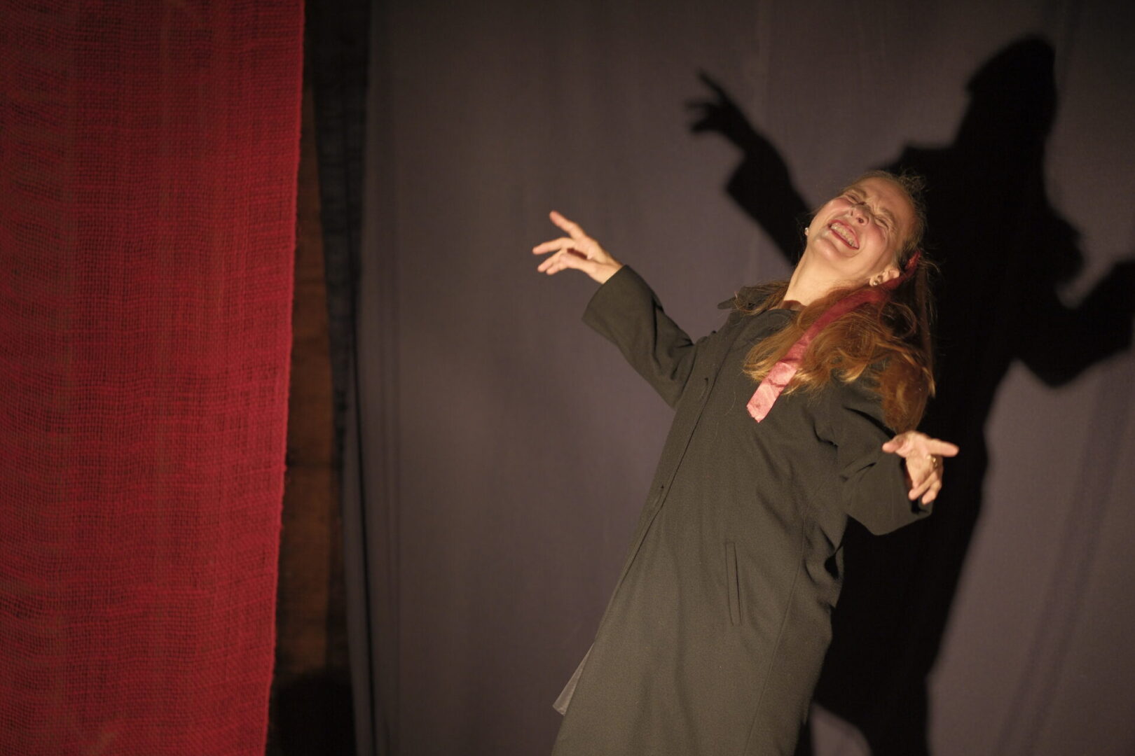 Older adult woman with dramatic gestures on theatrical stage. Woman performing with dramatic shadow backdrop.